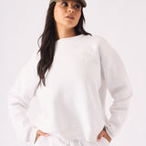 A front view of a woman wearing a white crew neck jumper and matching joggers with a khaki cap