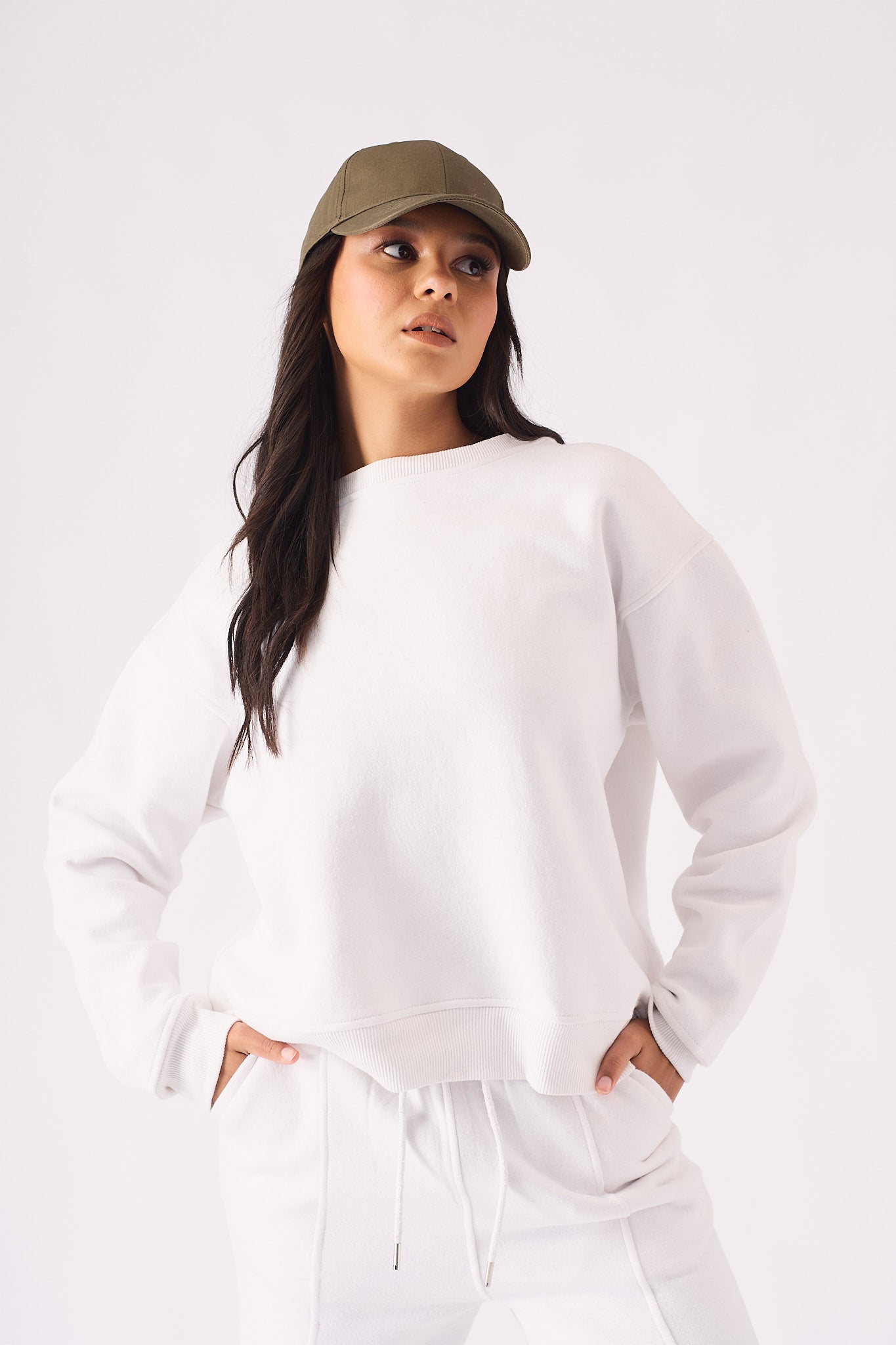 A front view of a woman wearing a white crew neck jumper and matching joggers with a khaki cap