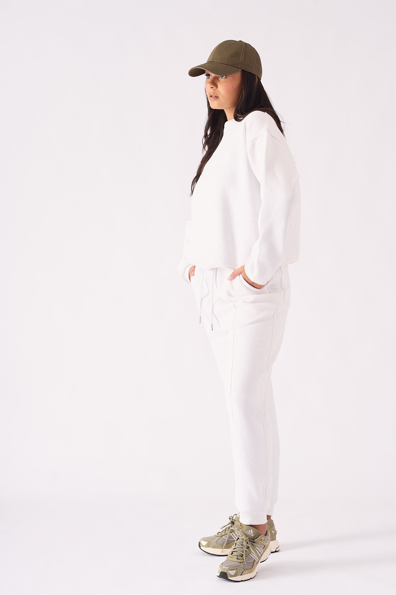 A side view of an oversized white crew neck jumper for women styled with a casual cap