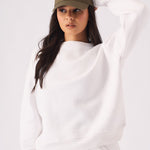 A woman posing in a white crew neck jumper while holding her cap for a sporty style