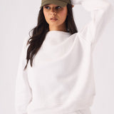 A woman posing in a white crew neck jumper while holding her cap for a sporty style
