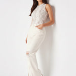 Model leaning against a wall wearing high-rise distressed white jeans with split hems and sunglasses.