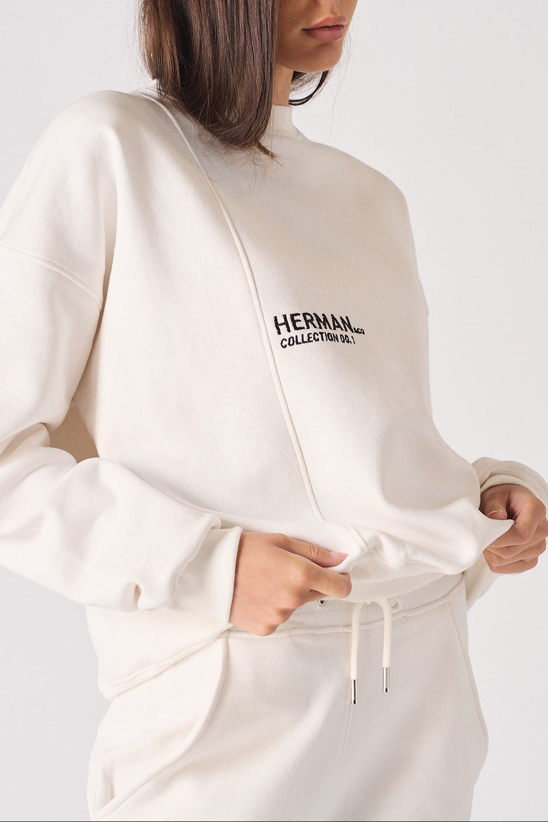 A woman holding the bottom hem of a white sweatshirt for women