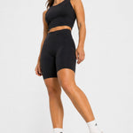 Full body shot of a woman modelling a black athleisure racer neck crop top and biker shorts.