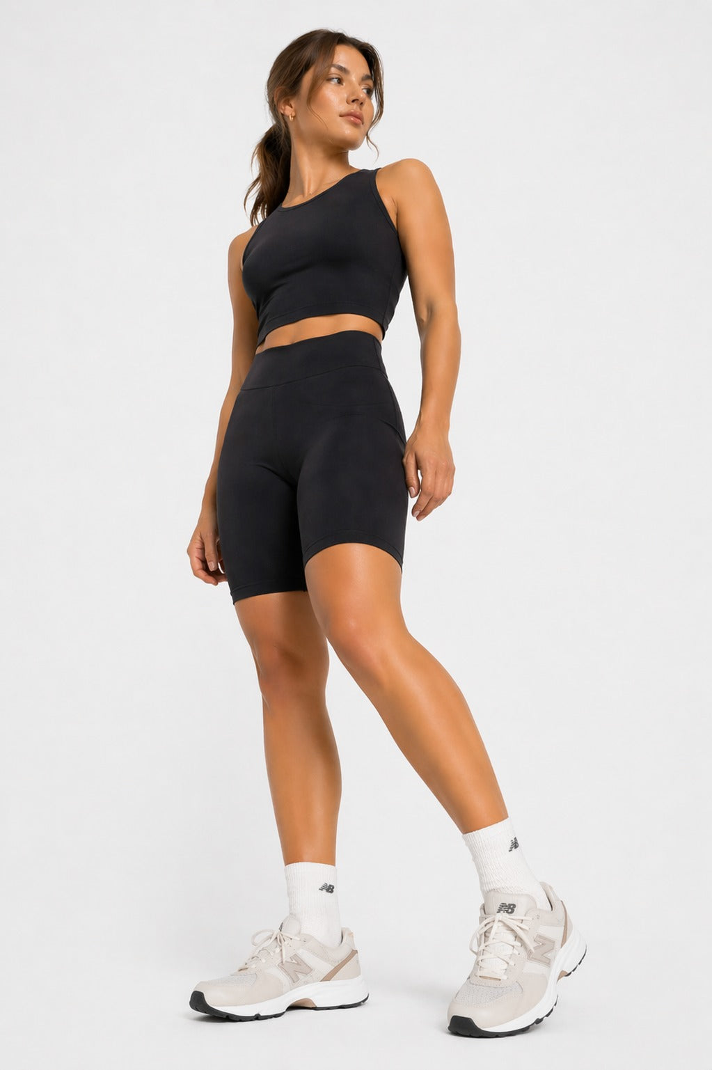 Full body shot of a woman modelling a black athleisure racer neck crop top and biker shorts.
