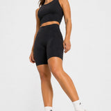 Full body shot of a woman modelling a black athleisure racer neck crop top and biker shorts.