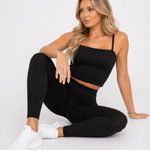 A woman seated on the floor wearing womens-black-bubble-texture-leggings styled with a matching black crop top and white trainers