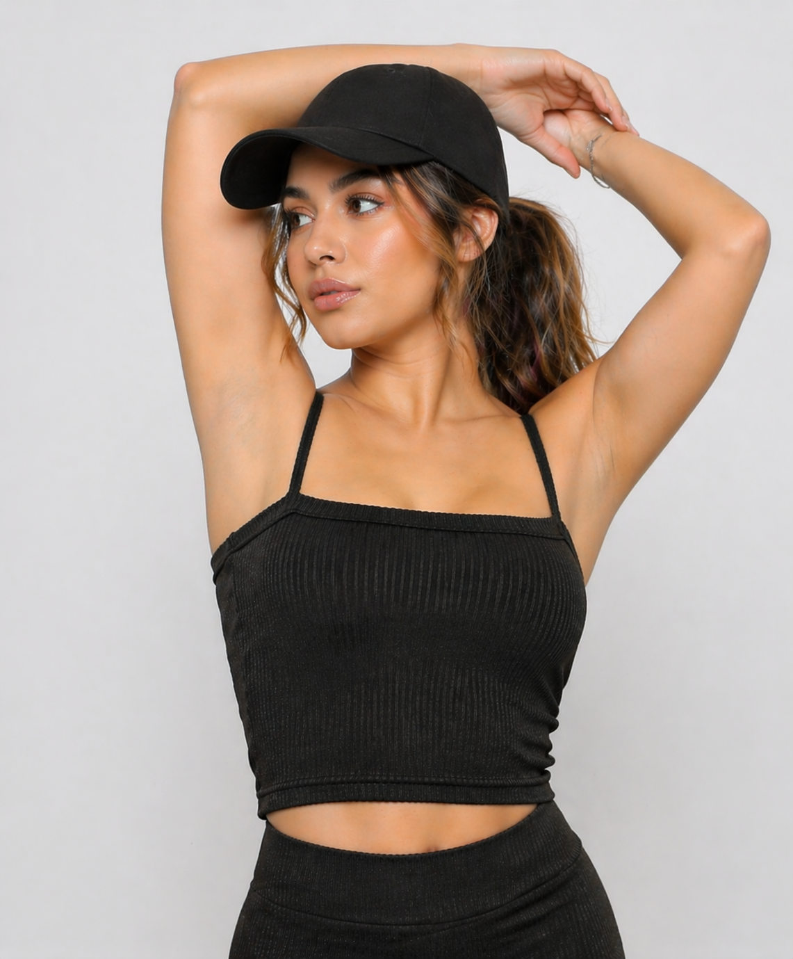 A woman wearing womens-black-ribbed-crop-top with arms raised showing the thin cami straps and natural support