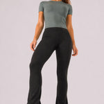 A woman wearing womens-black-kick-flare-leggings front view showing the wide high waistband and kick flare silhouette, styled with a green crop tee