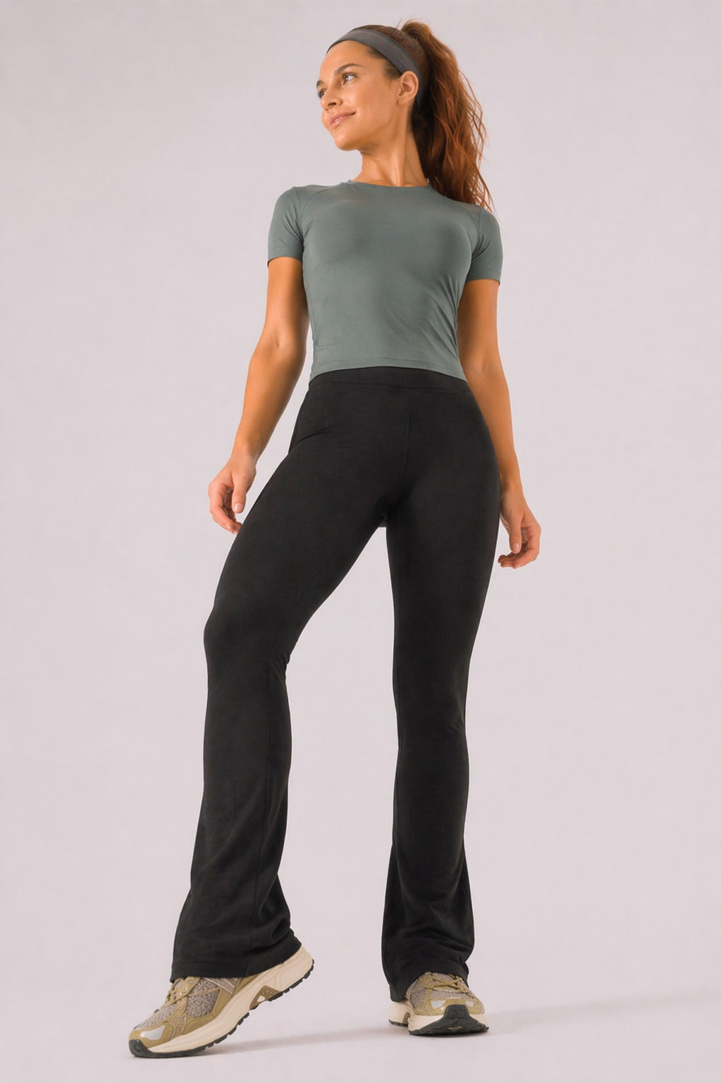 A woman wearing womens-black-kick-flare-leggings front view showing the wide high waistband and kick flare silhouette, styled with a green crop tee
