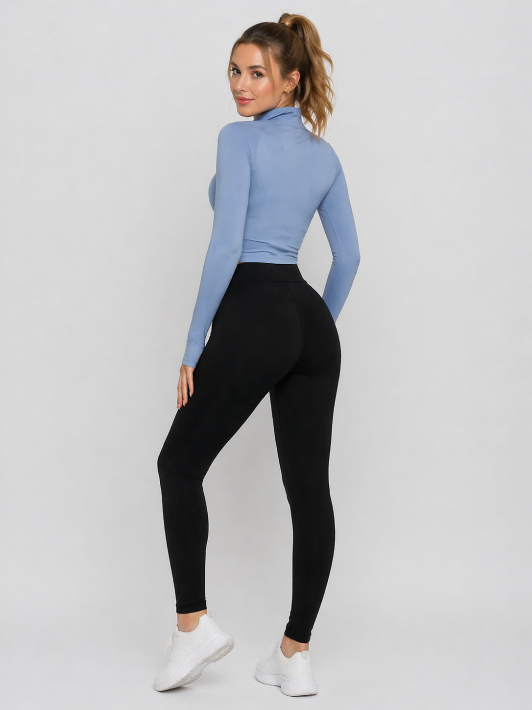 A woman wearing womens-black-high-waist-leggings with a deep waistband, showing the back fit and shape, paired with a blue crop top