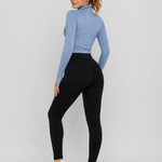 A woman wearing womens-black-high-waist-leggings with a deep waistband, showing the back fit and shape, paired with a blue crop top