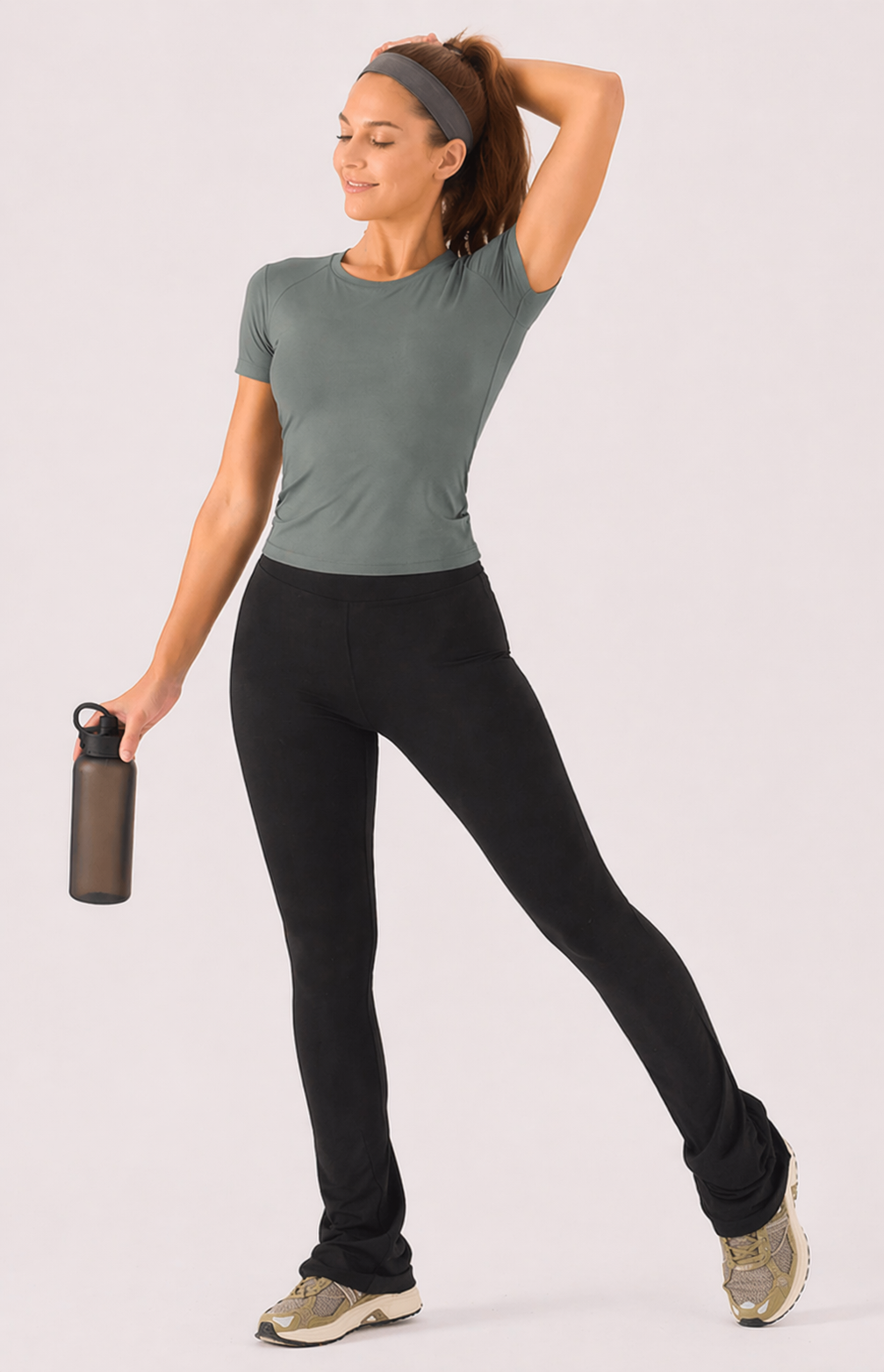 A woman wearing womens-black-kick-flare-leggings with high waist holding a water bottle in an active pose, styled with a green crop tee and headband
