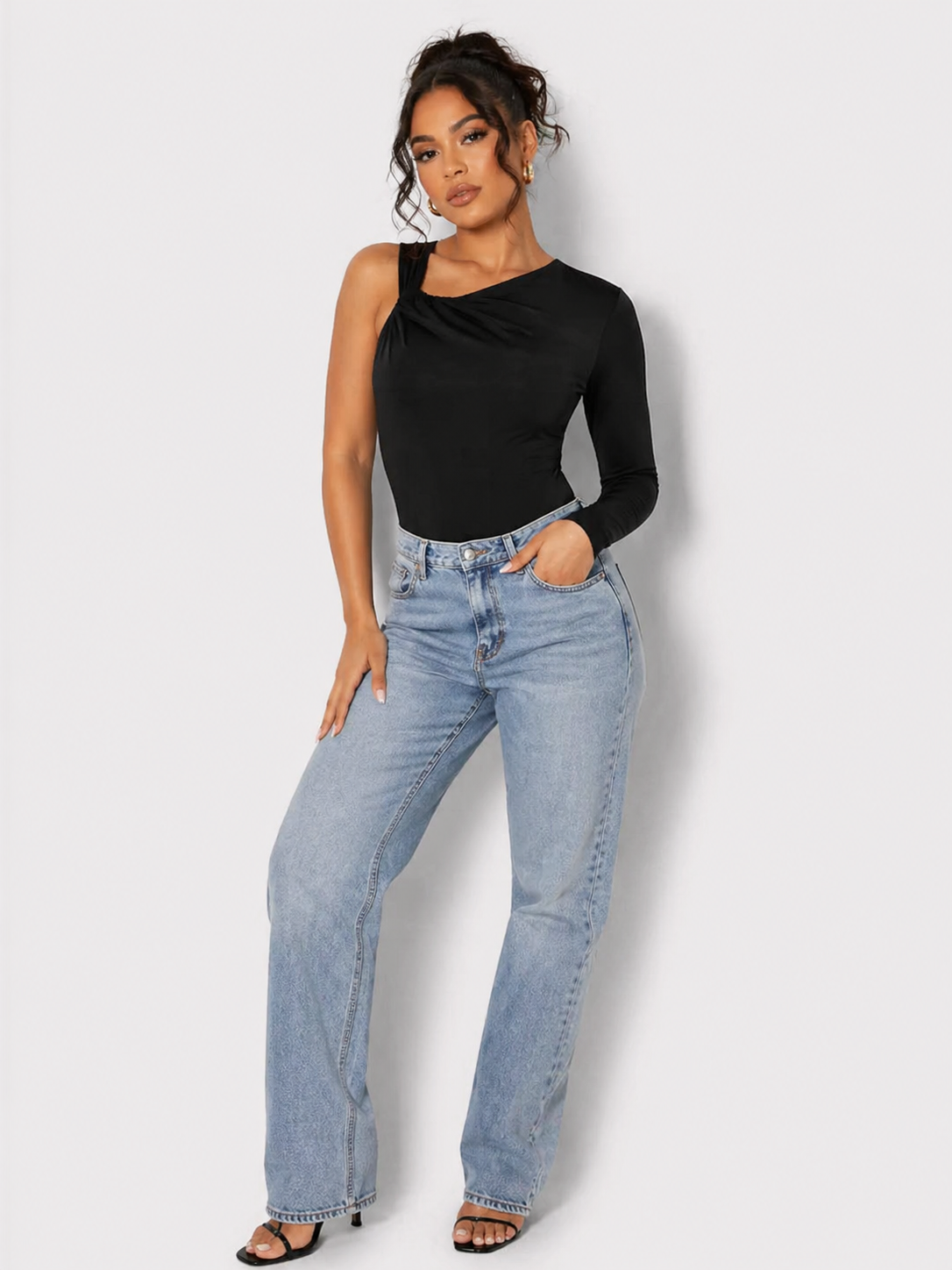 A woman standing full length wearing a Women's Black One Shoulder Ruched Bodysuit with blue jeans and black heels