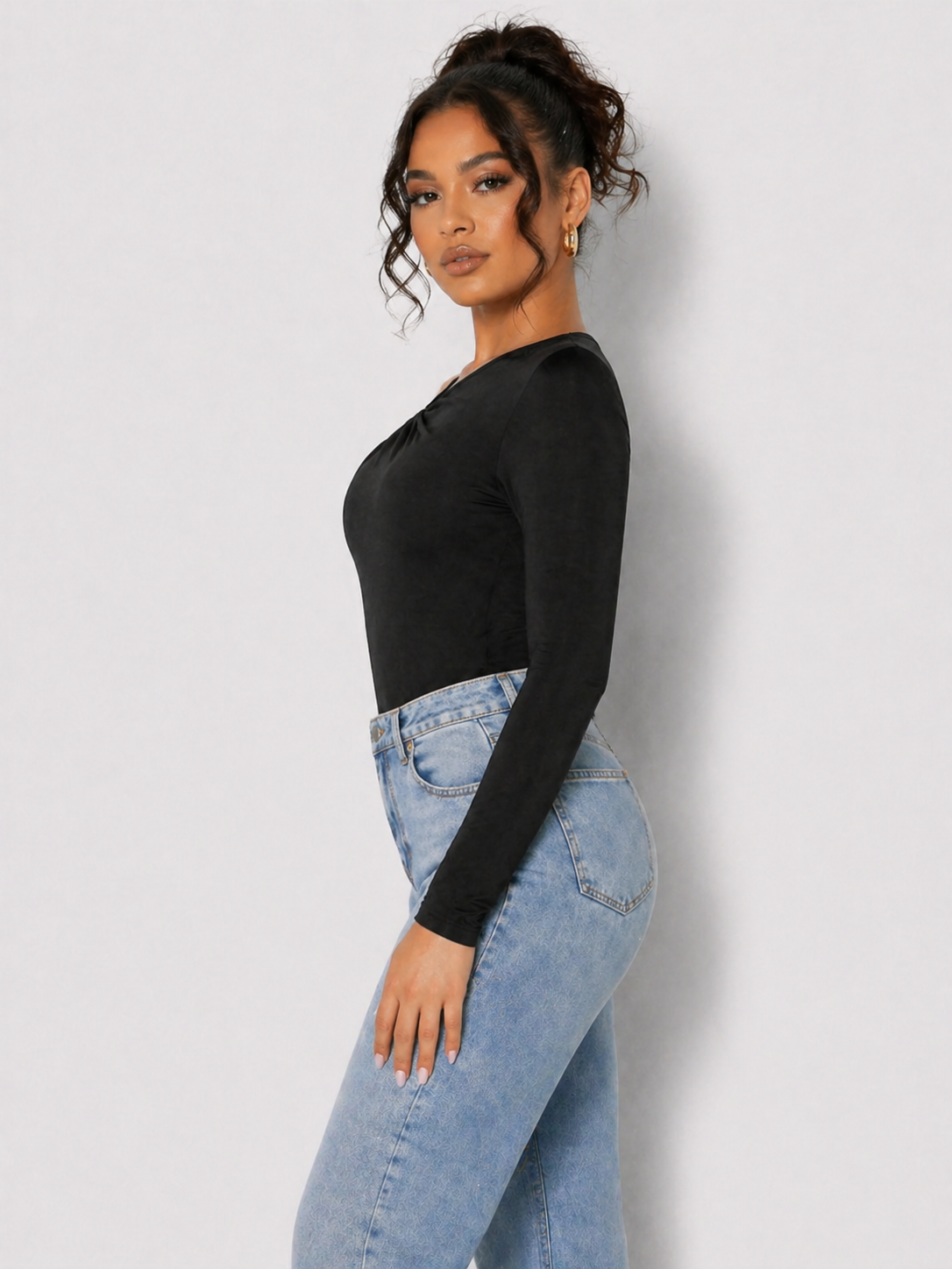 Side view of a woman in a Women's Black One Shoulder Ruched Fitted Bodysuit with blue jeans