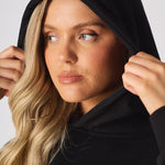 A woman posing with arms crossed wearing a black oversized hoodie