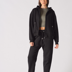A model wearing women's black tapered joggers with a matching zip hoodie.