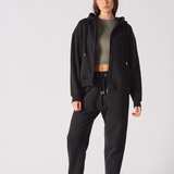 A model wearing women's black tapered joggers with a matching zip hoodie.