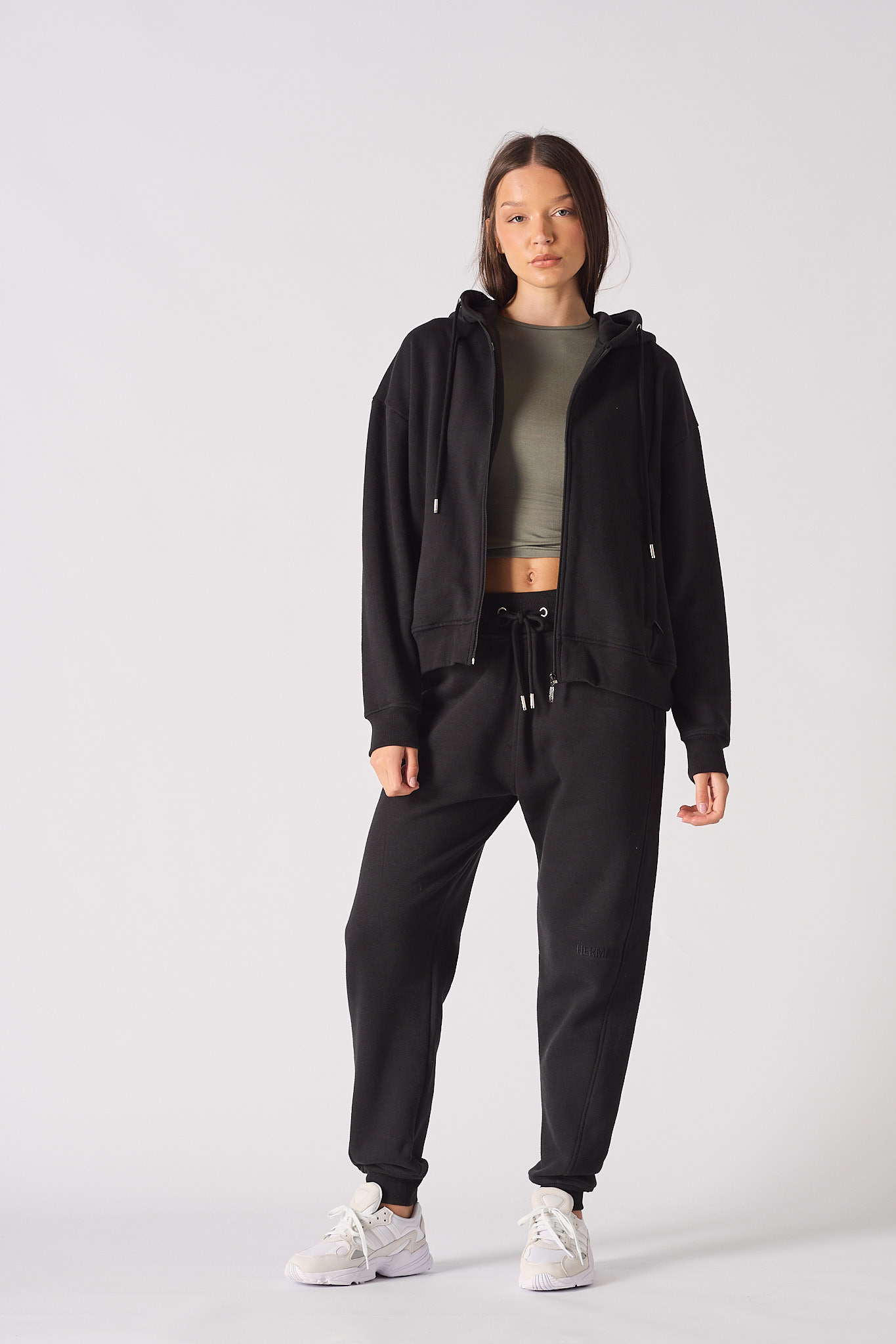 A model wearing women's black tapered joggers with a matching zip hoodie.