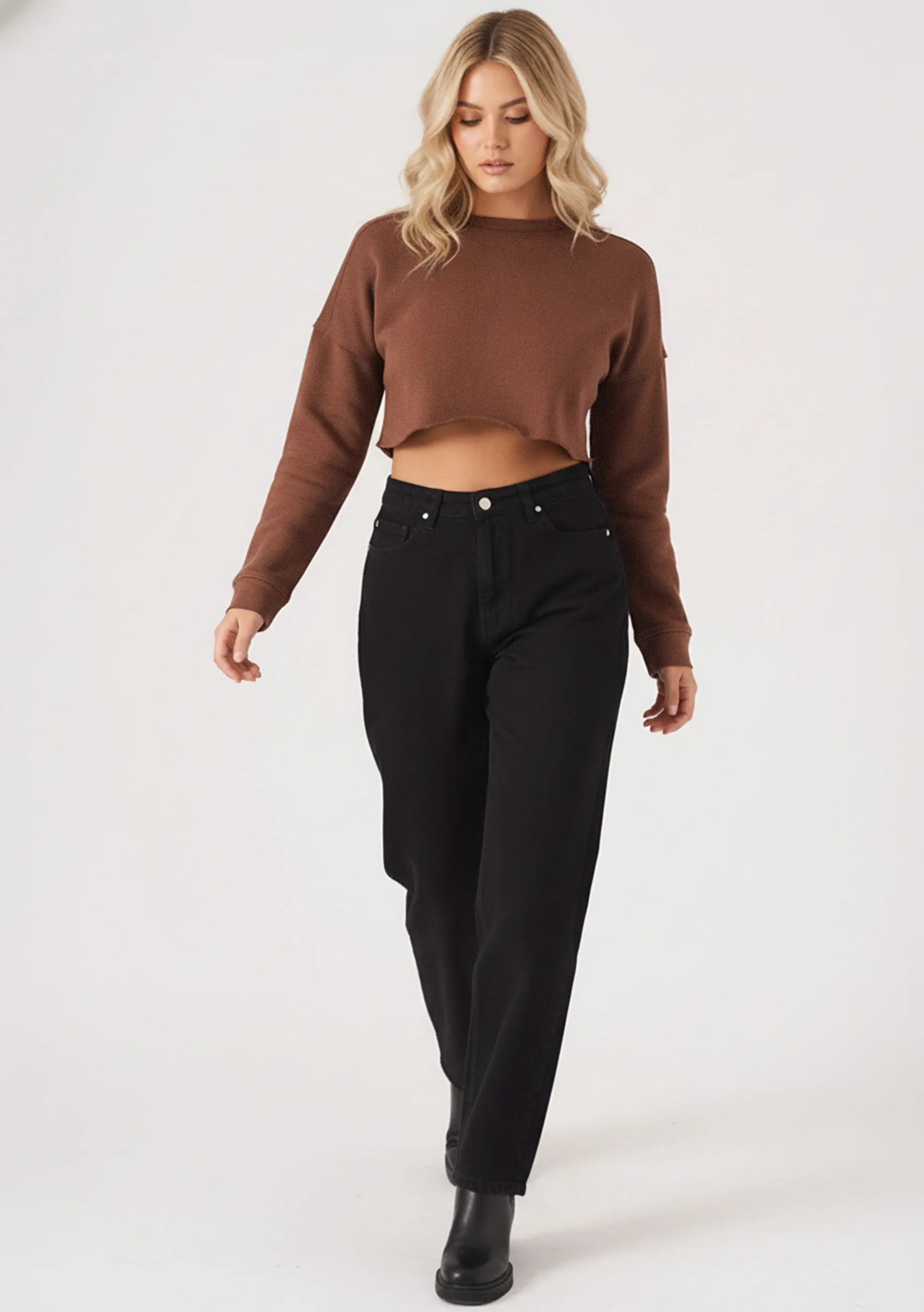 A full length front view of a model styling a brown cropped jumper with casual black trousers