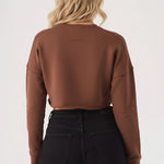 Rear angle view of a model in a brown cropped jumper and black trousers