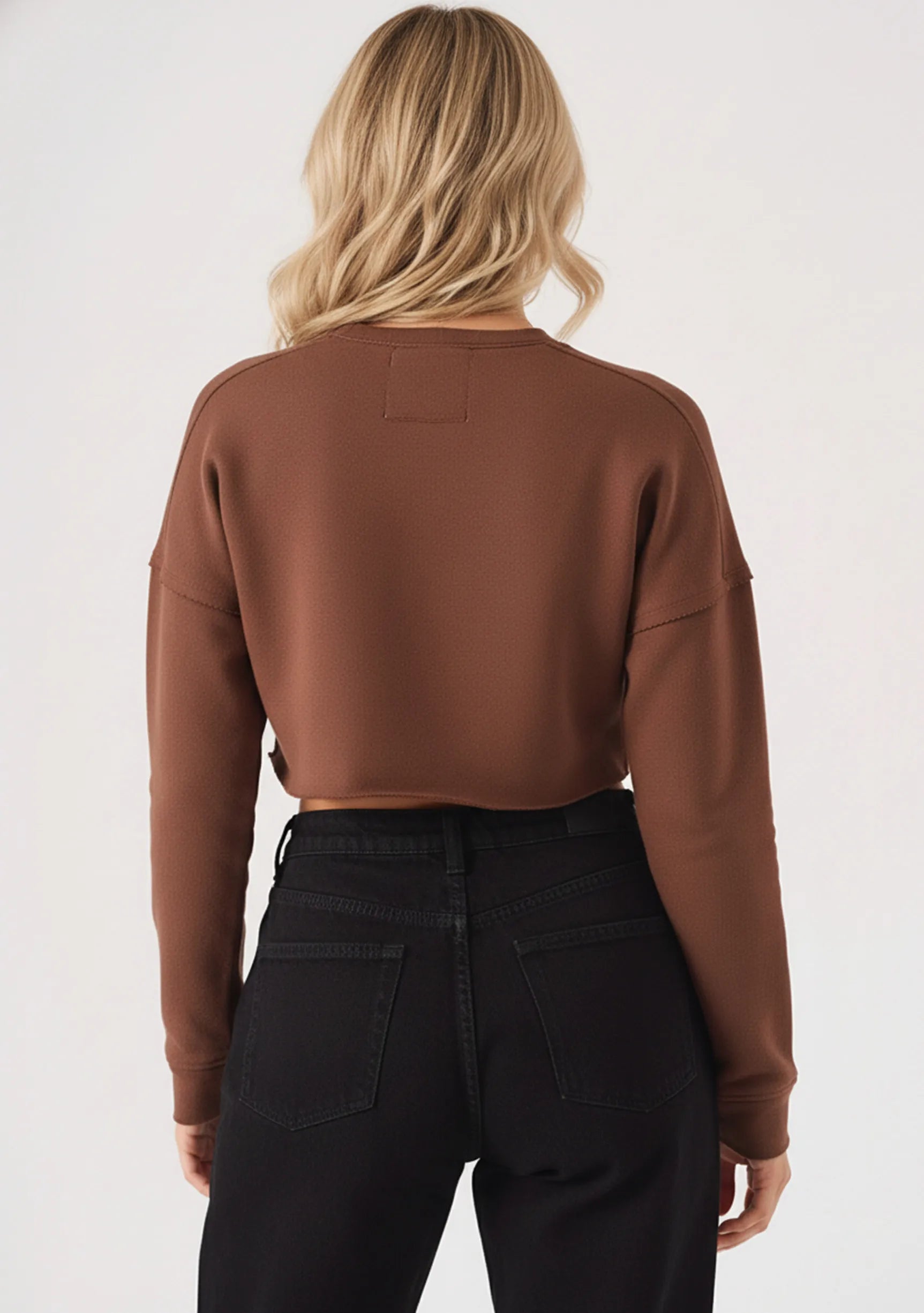 Rear angle view of a model in a brown cropped jumper and black trousers