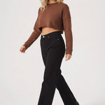 Side profile of a woman walking while wearing a brown cropped jumper and black wide leg jeans