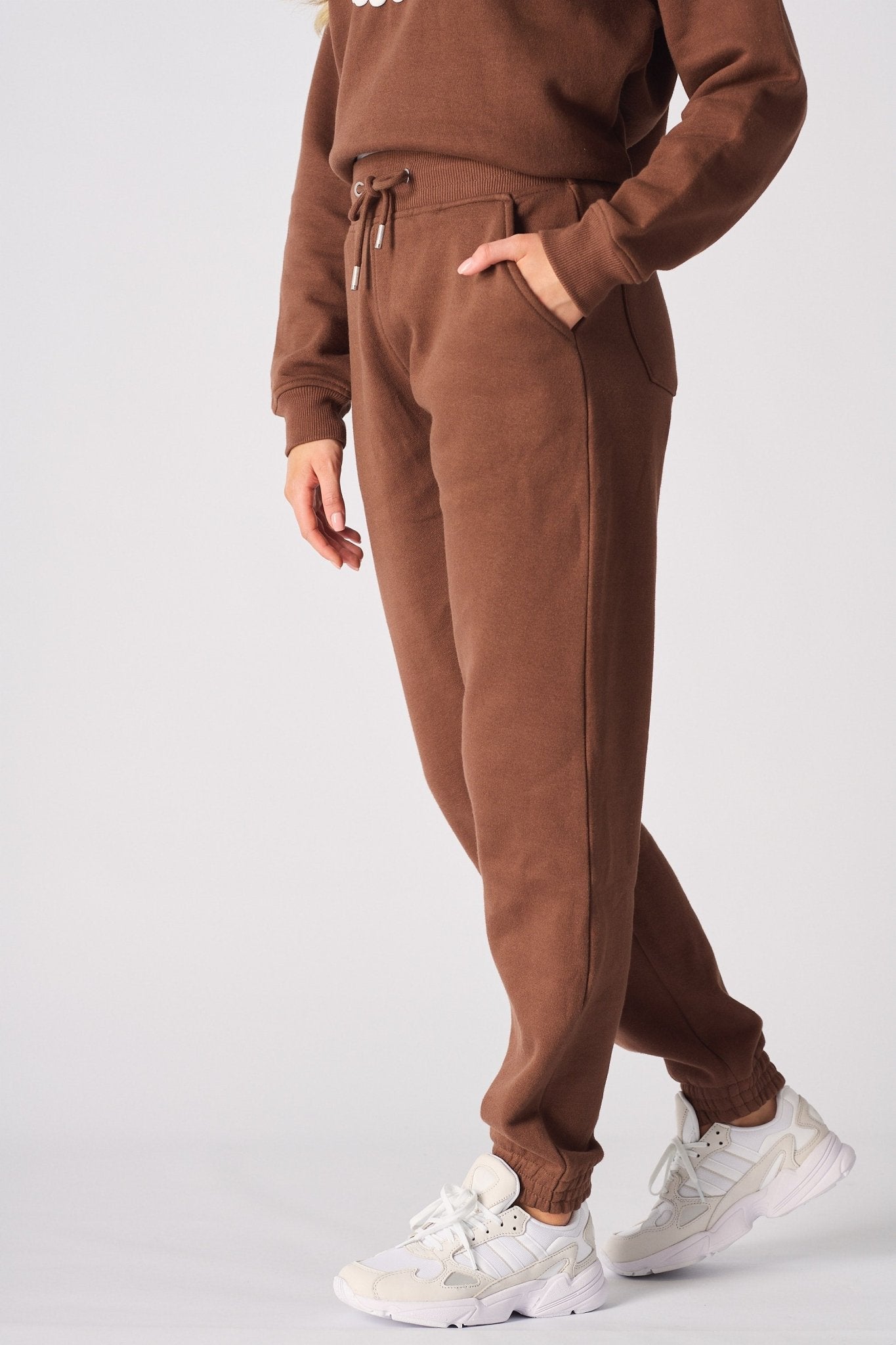 Side profile of a woman walking in brown cuffed joggers and white trainers