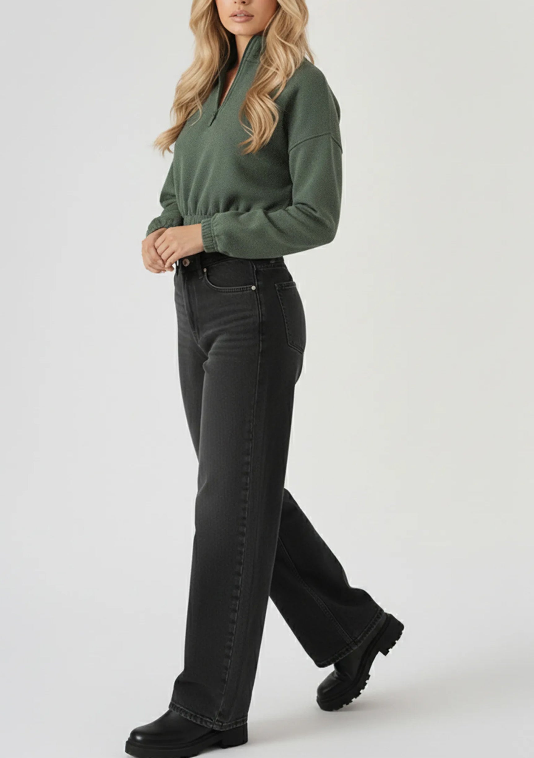 Full side length view of a woman styling a green half zip sweatshirt with black wide leg trousers