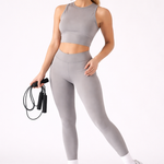 A woman wearing womens-grey-high-waist-butt-lifting-leggings holding a skipping rope, front view styled with a matching grey crop top and cream cap