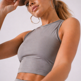 A woman wearing womens-grey-racerback-training-crop-top in a dynamic movement pose showing the stretch and fit