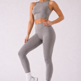 A woman wearing womens-grey-racerback-training-crop-top full length view styled with matching grey leggings and a cream cap