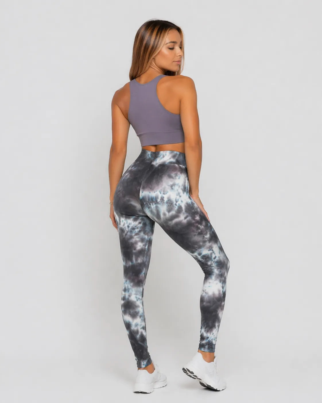A woman wearing womens-grey-tie-dye-high-waist-leggings back view showing the fit and print detail, paired with a purple crop top
