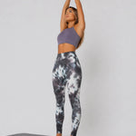 A woman in womens-grey-tie-dye-high-waist-leggings standing on a yoga mat with arms raised above head, side view showing full length fit