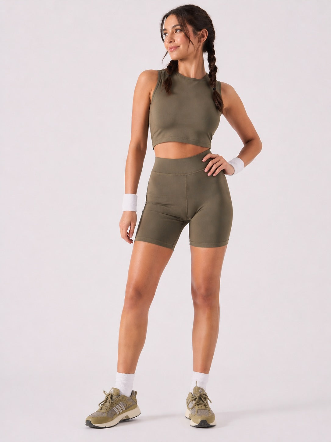 A woman wearing womens-khaki-high-waist-biker-shorts full length front view styled with a matching khaki crop top and olive trainers