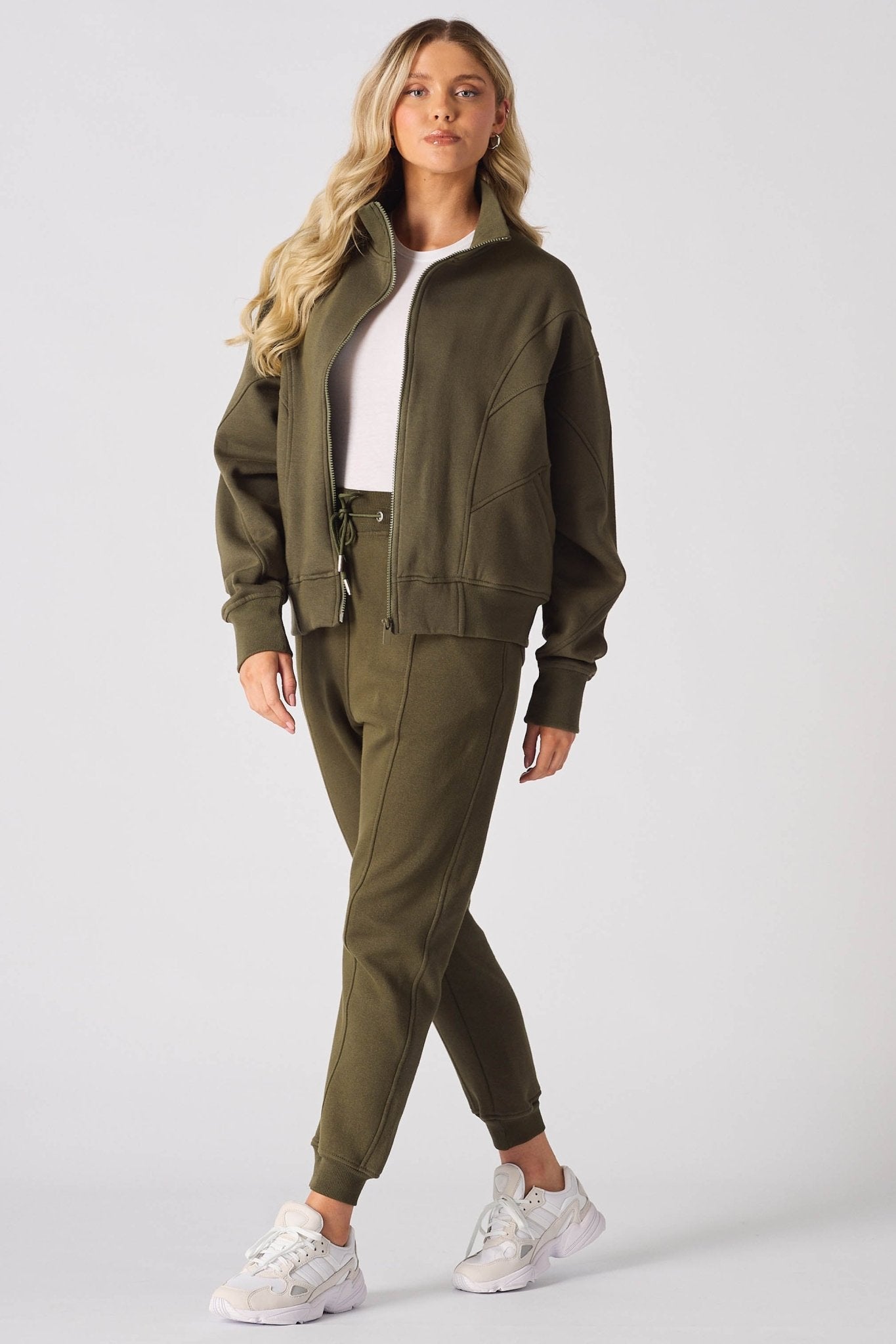 A woman standing in a complete khaki tracksuit set with white trainers