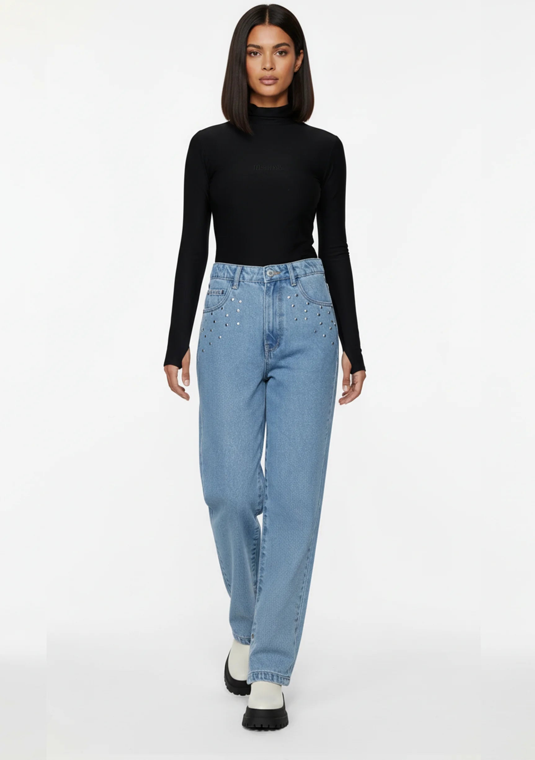 Front walking pose of a model wearing women's vintage wash denim pants featuring metallic pocket studs.