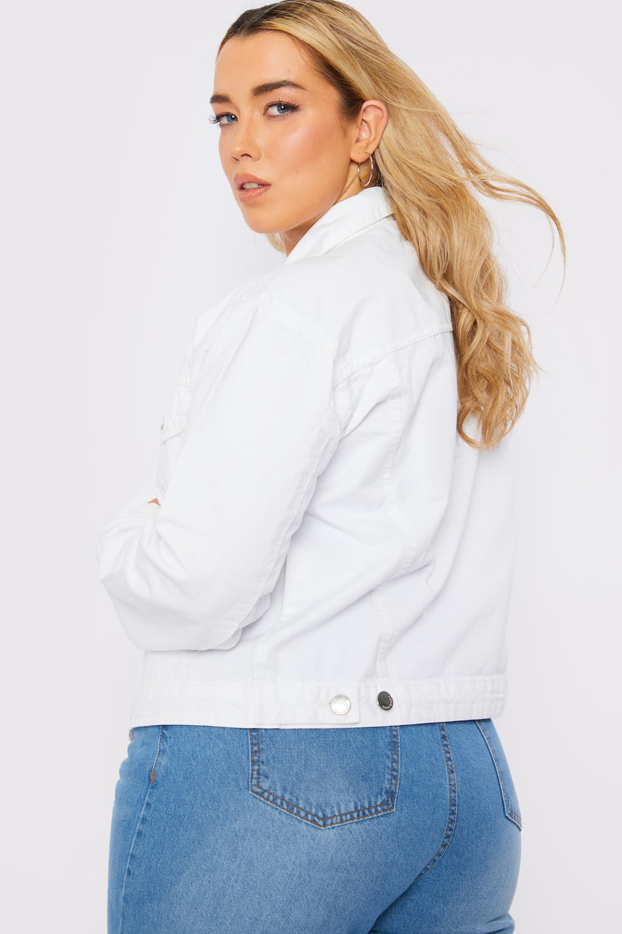 Side to back body shot of a standing plus size female model wearing a JMOJO White Denim Trucker Jacket