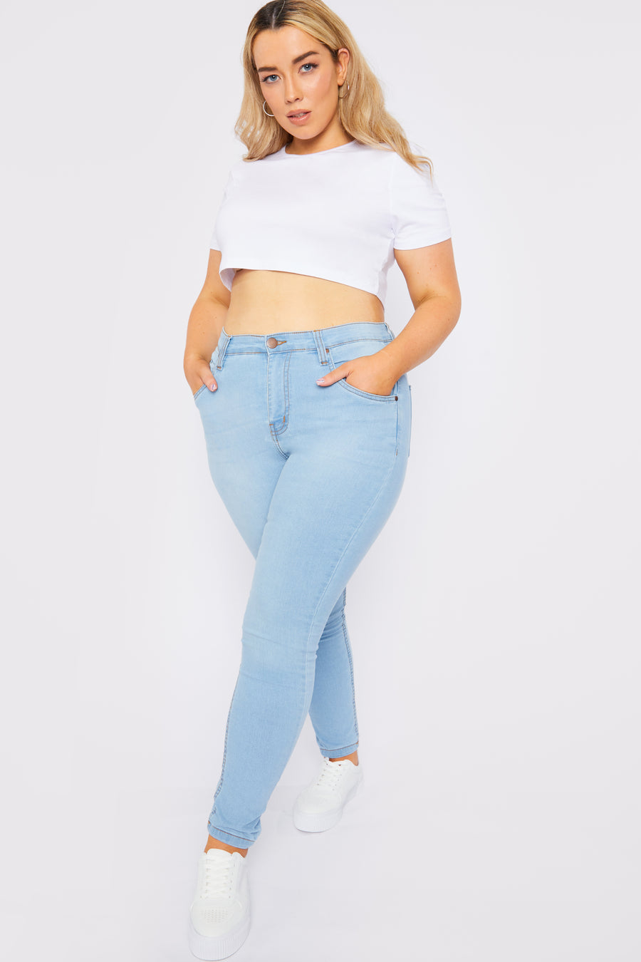 Full body shot of a plus size standing female model wearing JMOJO Plus Light Blue Wash High Waisted Skinny Jeans