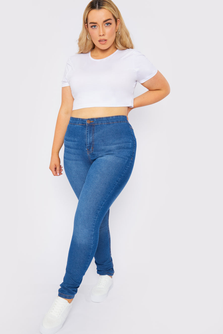 Full body shot of a standing plus size female model wearing JMOJO Mid Blue High Waisted Skinny Jeans