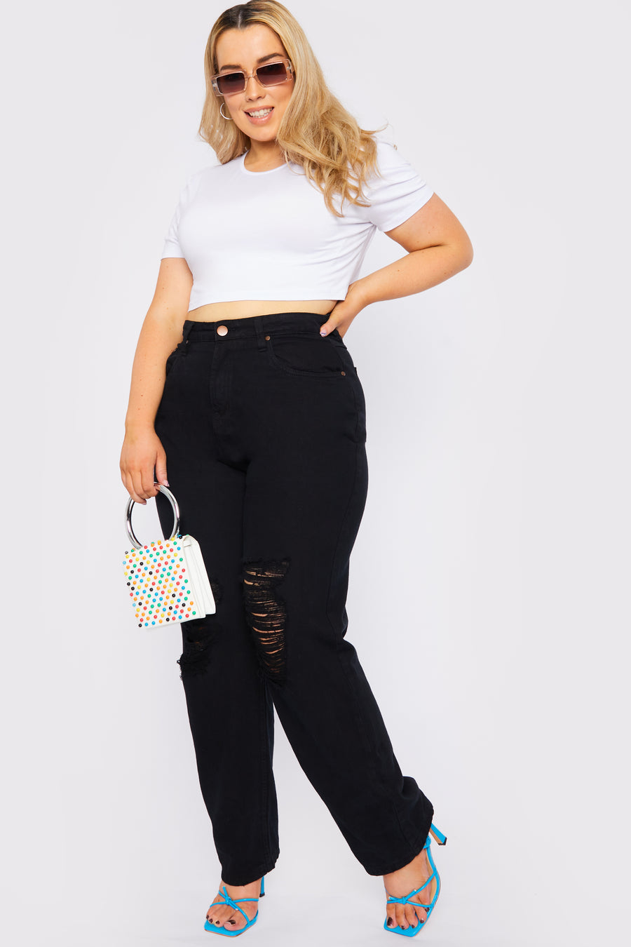 Full body style shot of a standing female plus size model wearing JMOJO Black High Waisted Straight Leg Ripped Jeans holding a handbag and wearing sunglasses