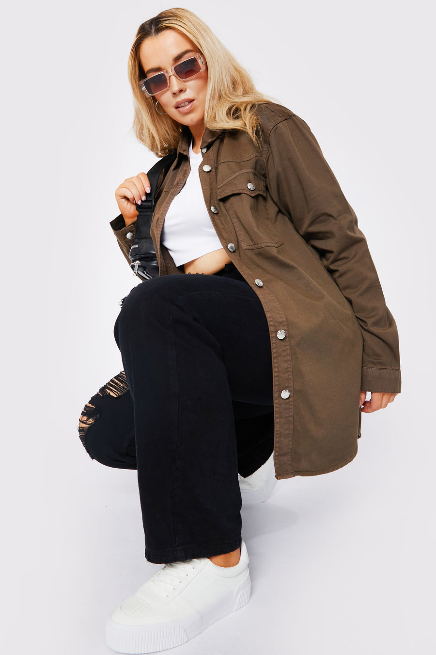 Full body style shot of a kneeling plus size female model wearing a JMOJO Brown Wash Long Sleeve Denim Shirt with a handbag over the shoulder and wearing sunglasses