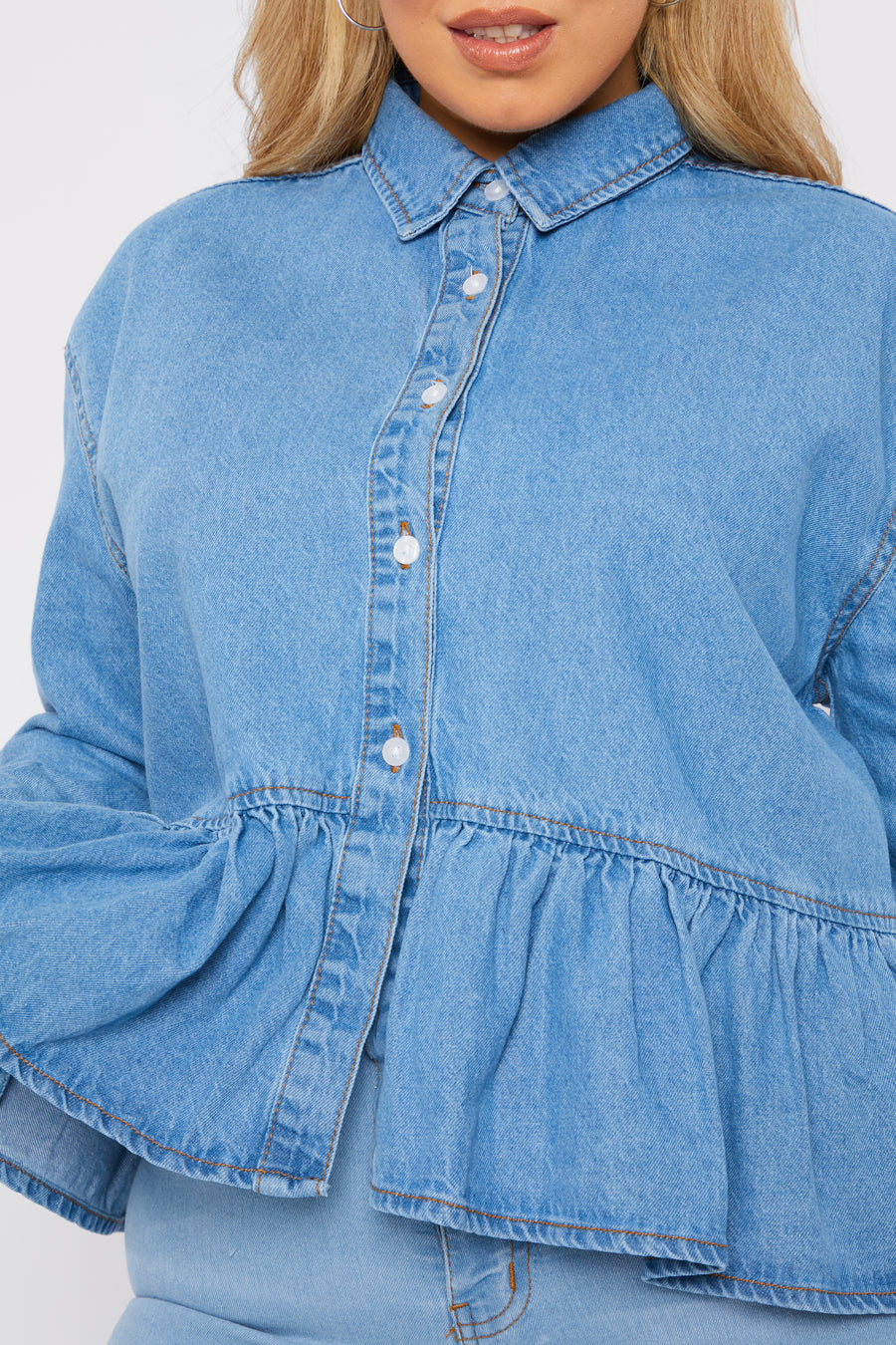 Close up product detail shot of a standing plus size female model wearing a JMOJO Light Blue Wash Peplum Denim Frill Shirt
