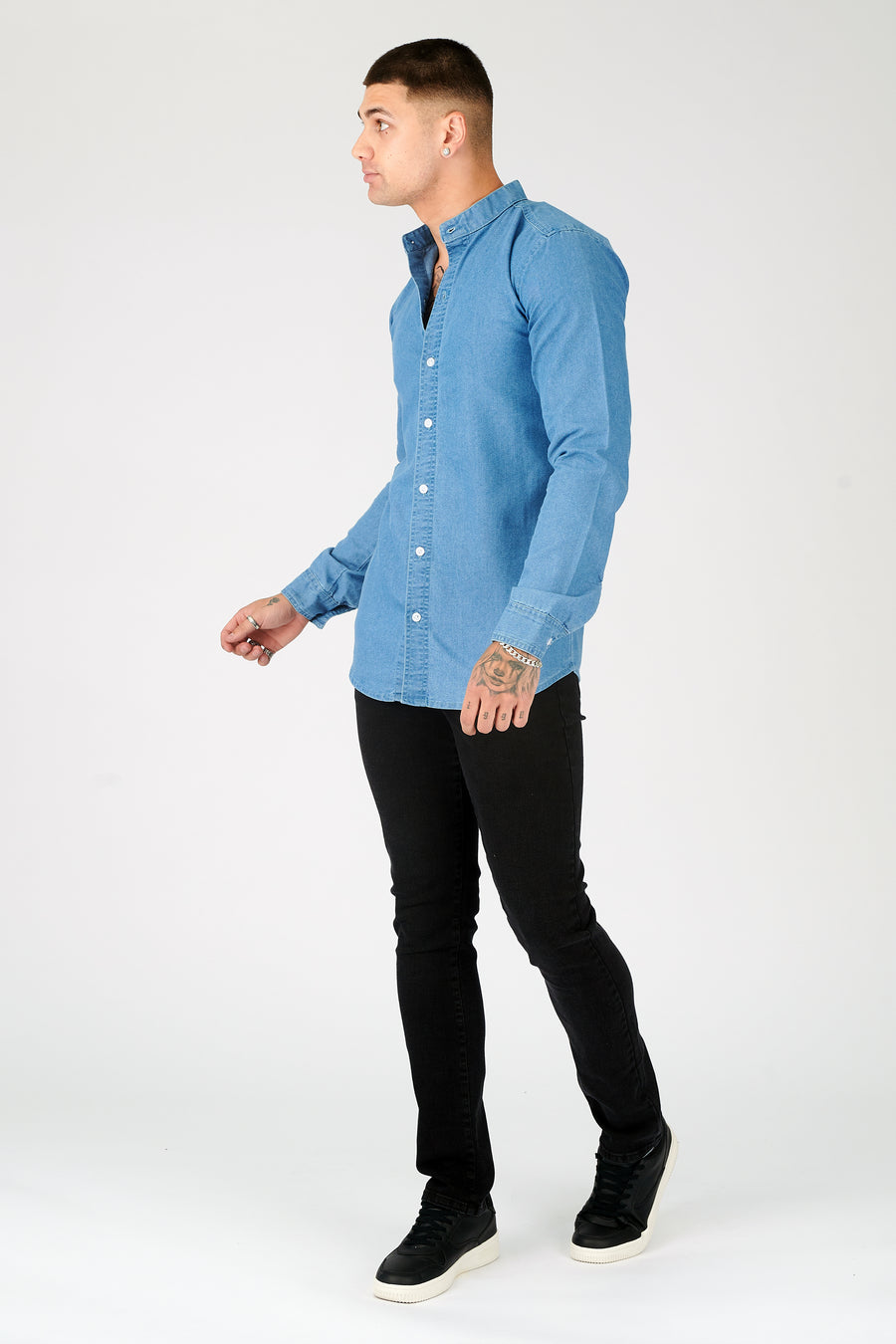 Body side shot of a standing male model wearing a JMOJO Blue Slim Fit Grandad Collar Denim Shirt