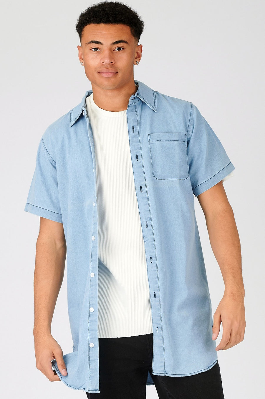 Close body shot of a standing male model wearing a JMOJO Light Blue Wash Slim Fit Longline Short Sleeve Denim Shirt