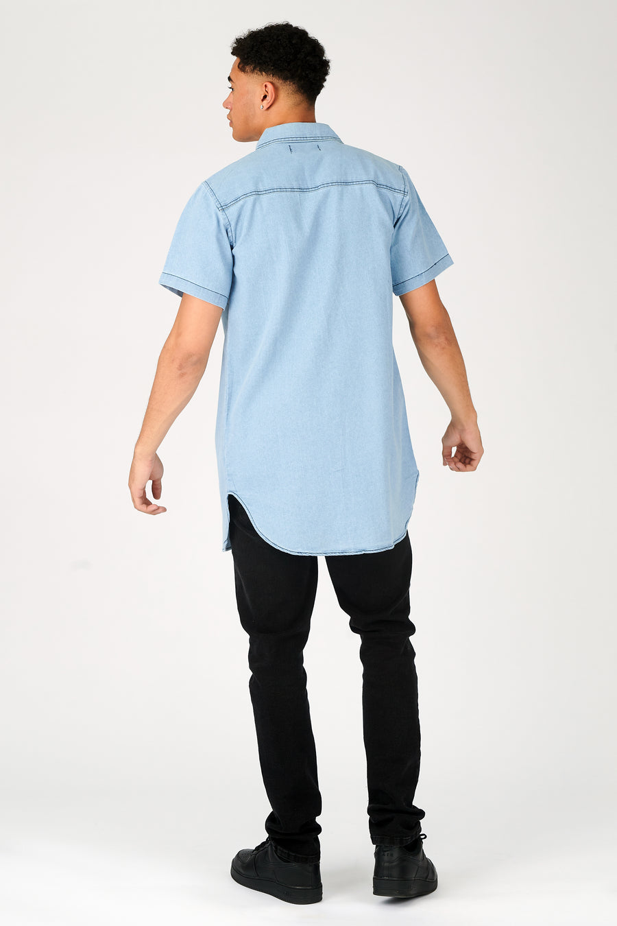 Body back  shot of a standing male model wearing a JMOJO Light Blue Wash Slim Fit Longline Short Sleeve Denim Shirt