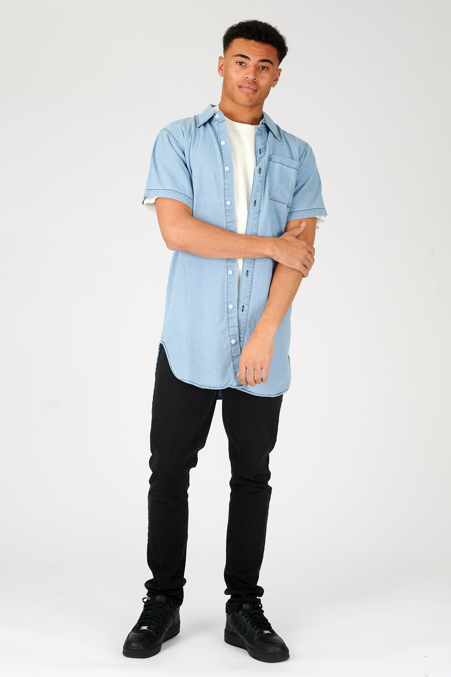 Body shot of a standing male model wearing a JMOJO Light Blue Wash Slim Fit Longline Short Sleeve Denim Shirt