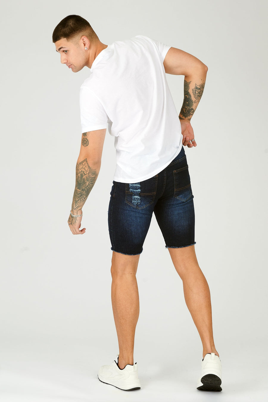 Body back shot of a standing male model wearing JMOJO Mid Blue Wash Slim Fit Ripped Denim Shorts