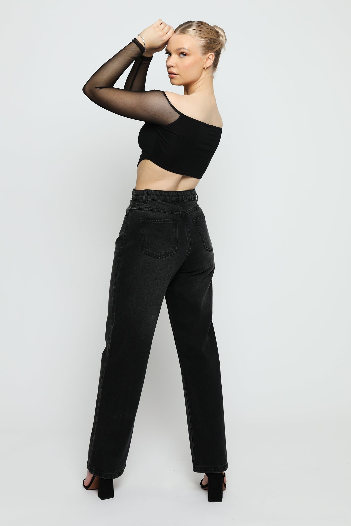 Rear view of a woman wearing relaxed black wide leg jeans showing the high-rise fit.