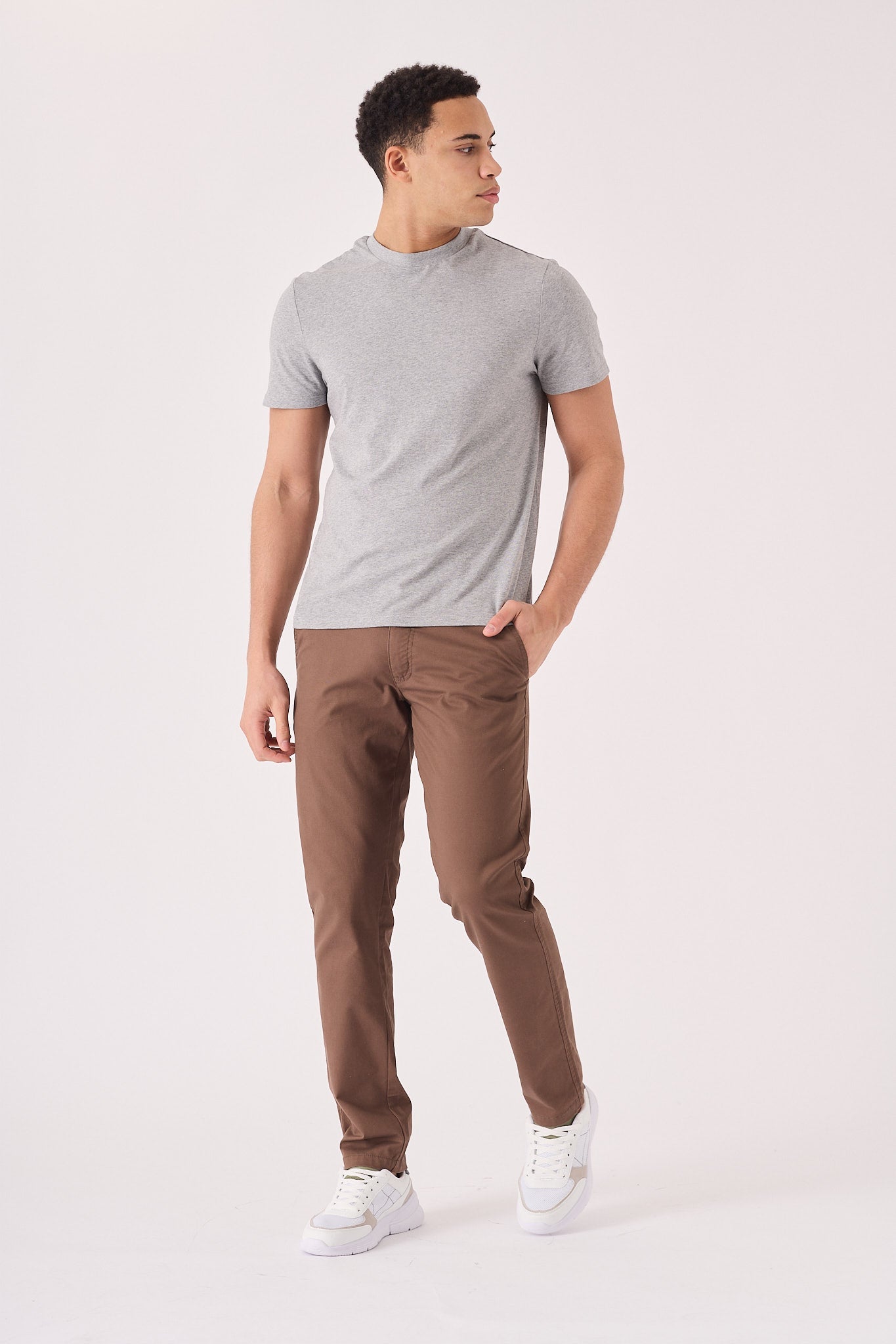 Full front view of a male model wearing slim brown chino trousers.